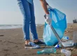 a person using a metal tong to pick up an empty bottled water on the beach