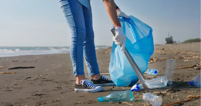 a person using a metal tong to pick up an empty bottled water on the beach