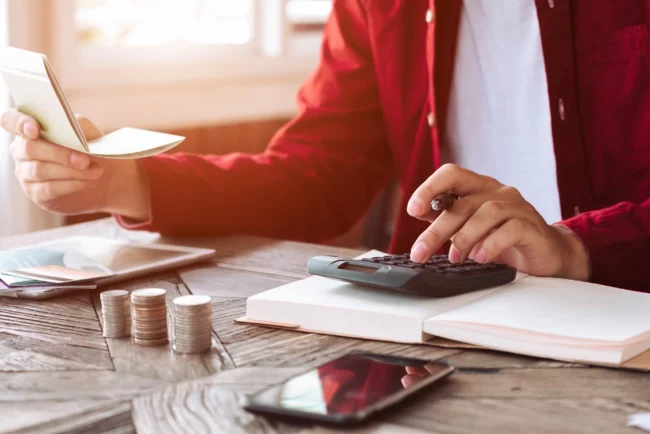 An image of a person doing budgeting. The person is holding paper receipts and using calculator with the other hand.