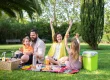 Parents with two kids having a picnic at the park, laughing and having fun.