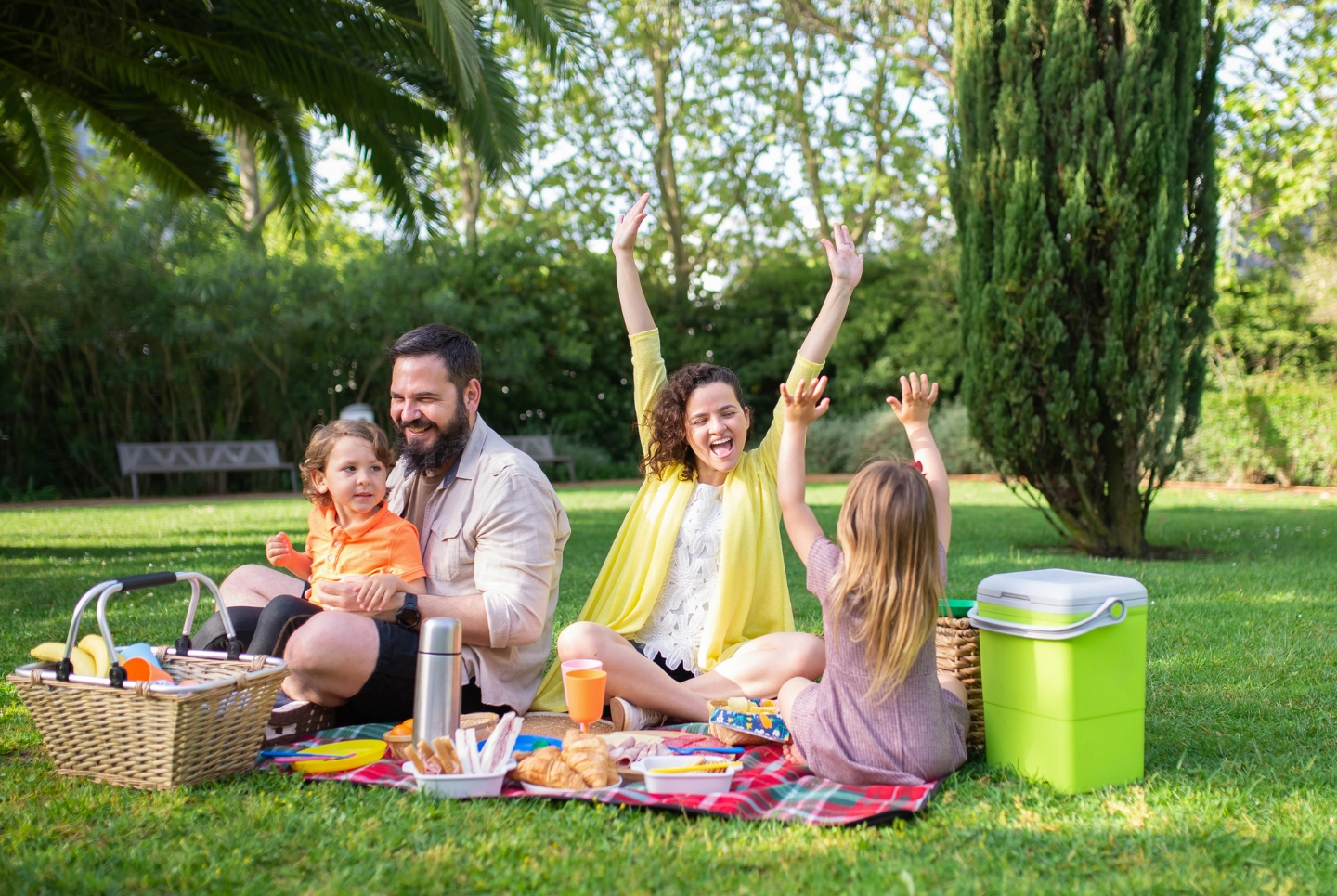 Parents with two kids having a picnic at the park, laughing and having fun.